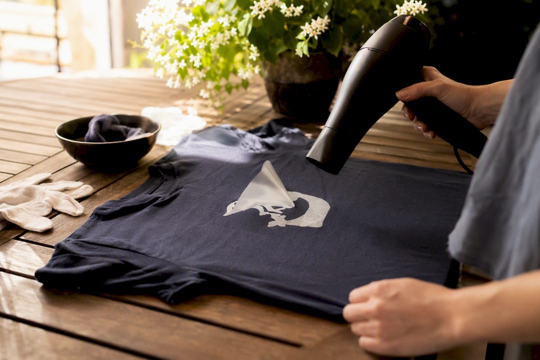 Hands applying heat to shirt for vinyl removal
